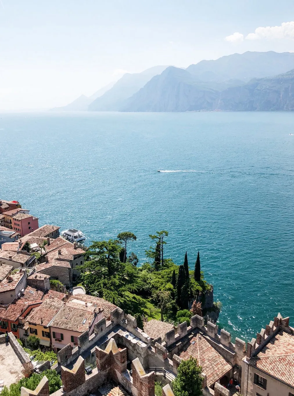 Ein malerischer Blick auf die Dächer von Malcesine am Gardasee, mit dem See und den Bergen im Hintergrund. Die rote Ziegelarchitektur und die grüne Landschaft bilden einen harmonischen Kontrast.