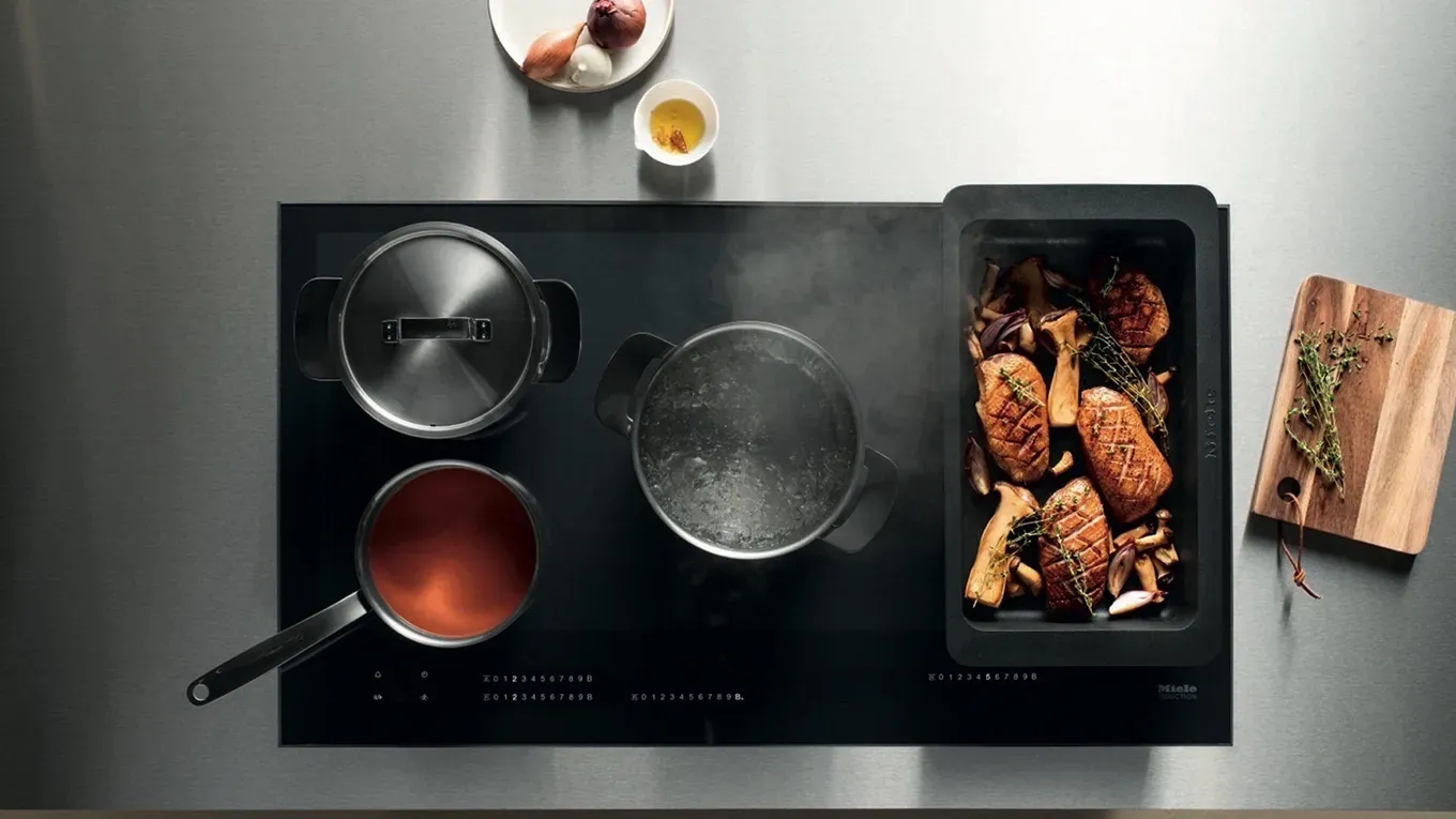 Ein Miele Induktionskochfeld mit FlexInduktion, bestückt mit verschiedenen Töpfen und Pfannen