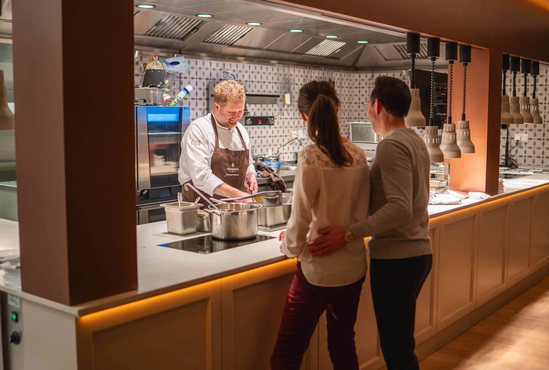 Ein Paar beobachtet den Koch bei der Zubereitung in der offenen Restaurantküche.