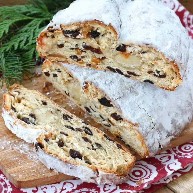 Ein perfekt gebackener, mit Puderzucker bestäubter Weihnachtsstollen auf einem Holzbrett, umgeben von weihnachtlicher Dekoration.