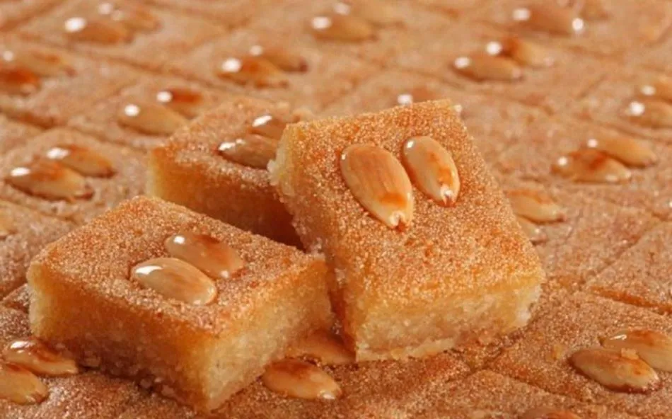 Ein quadratisches Stück Basboosa, ein leichter Grießkuchen, mit Zuckersirup getränkt und mit Mandeln garniert