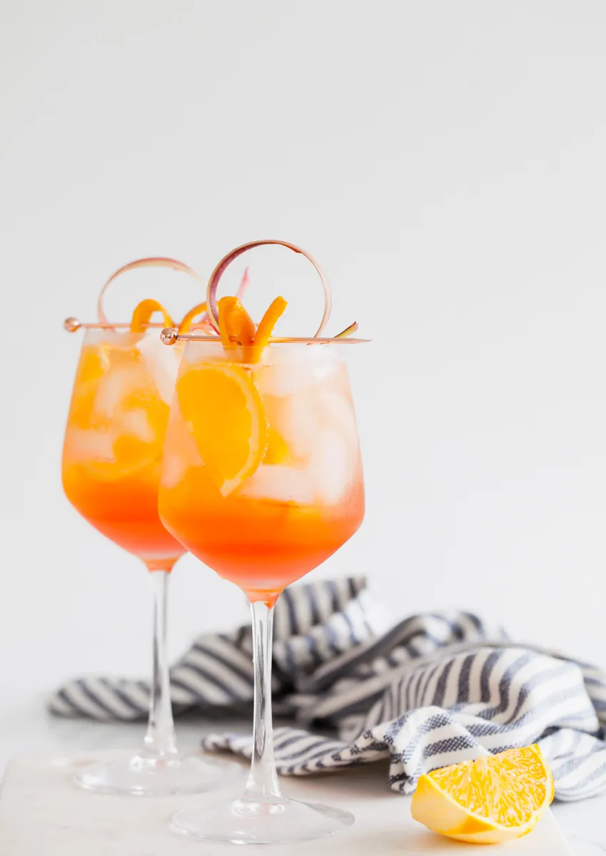 Ein Rhabarber Aperol Spritz mit Eis, Orangenzeste und Rhabarberdeko.