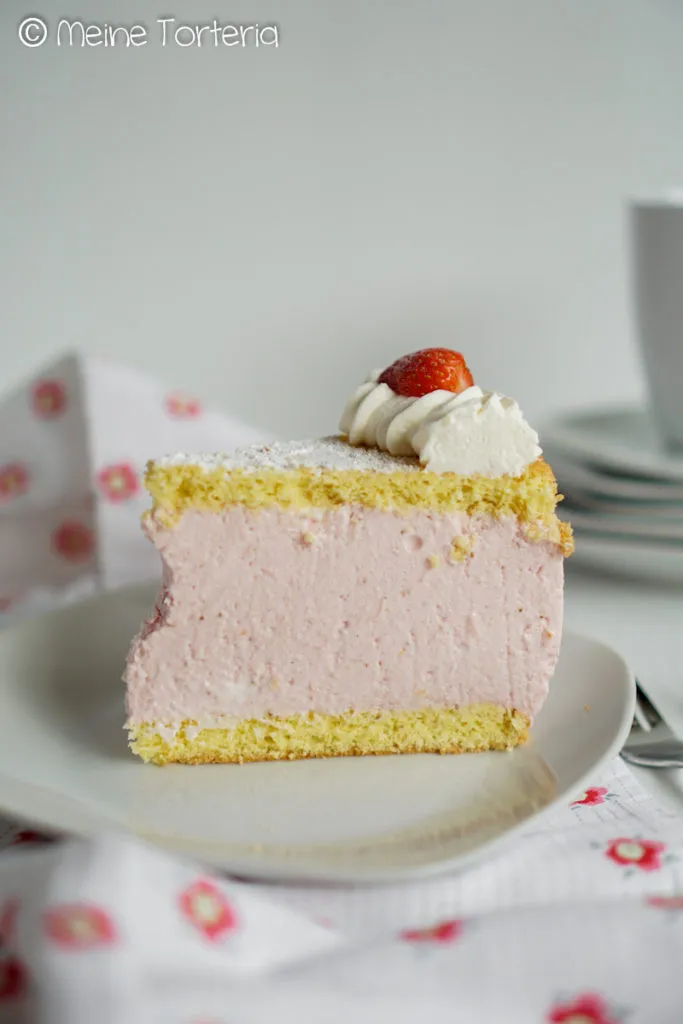 Ein schief geschnittenes Stück Erdbeer-Käsesahnetorte auf einem Teller