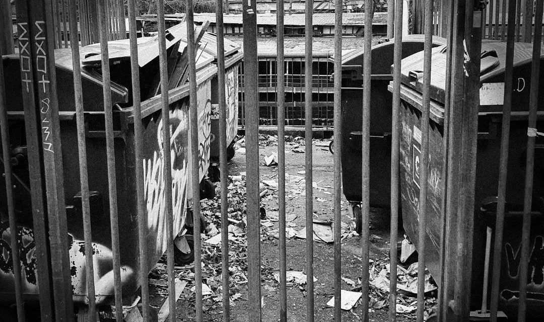 Ein schwarz-weißes Straßenbild in Berlin mit einem Gebäude, Menschen und einer Straßenbahnhaltestelle