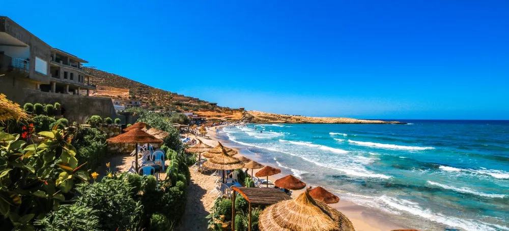 Ein sonniger Strand mit türkisfarbenem Wasser und Palmen in einem günstigen Urlaubsland.