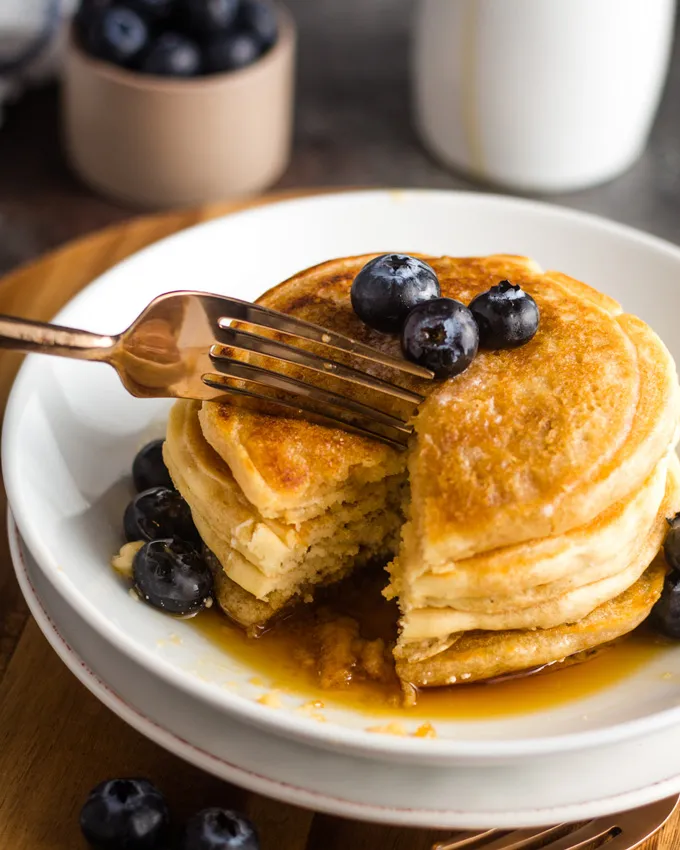 Ein Stapel Pancakes auf einem weißen Teller mit einer goldenen Gabel, die einen Bissen abschneidet.
