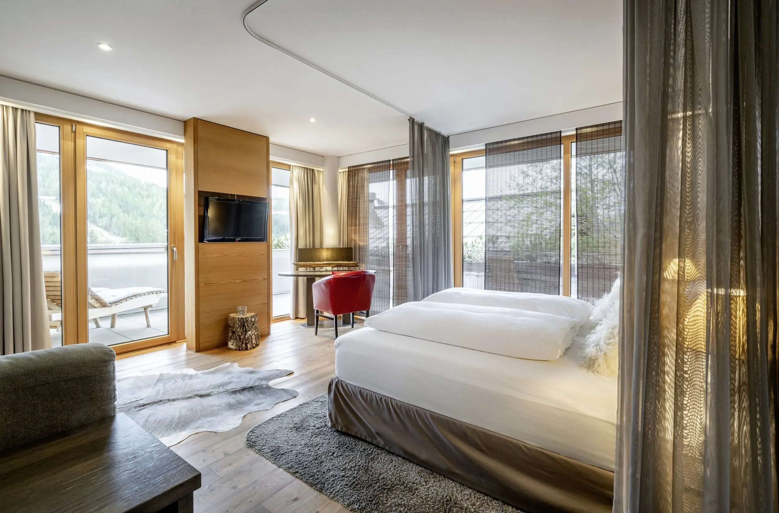 Ein stilvolles Doppelzimmer im HUBERTUS Mountain Refugio Allgäu, ausgestattet für Gäste und ihren Hund, mit großen Fenstern und gemütlichen Fellen.