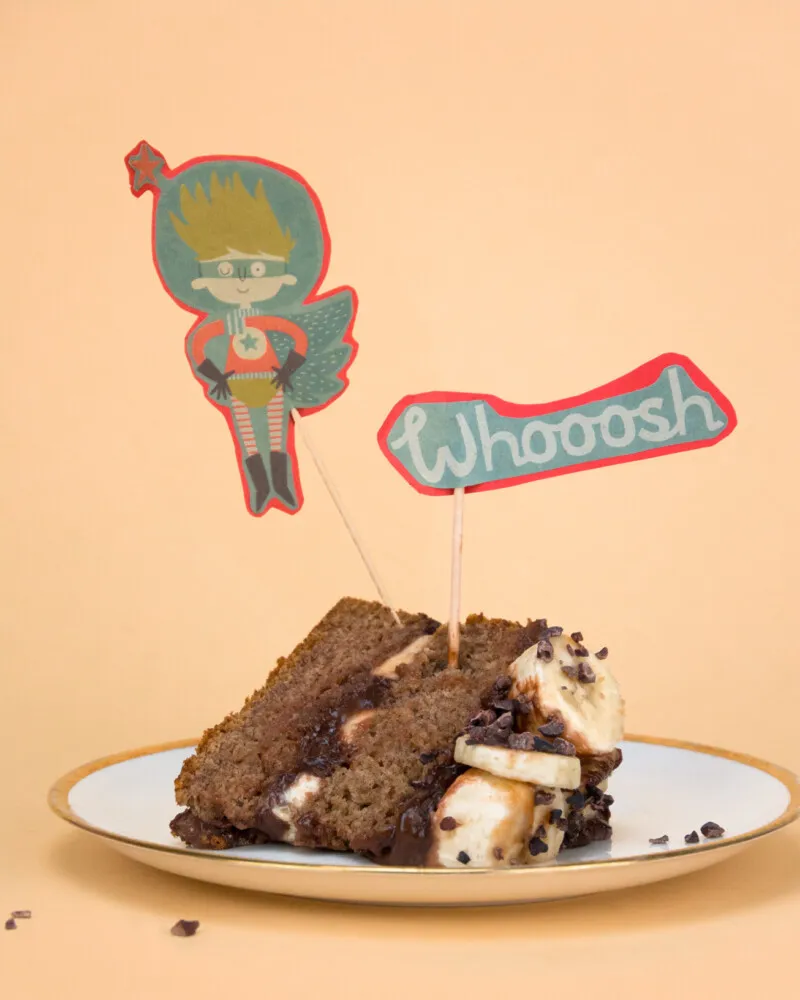 Ein Stück des gesunden Schoko-Geburtstagskuchens, belegt mit frischen Bananenscheiben und Kakaonibs.