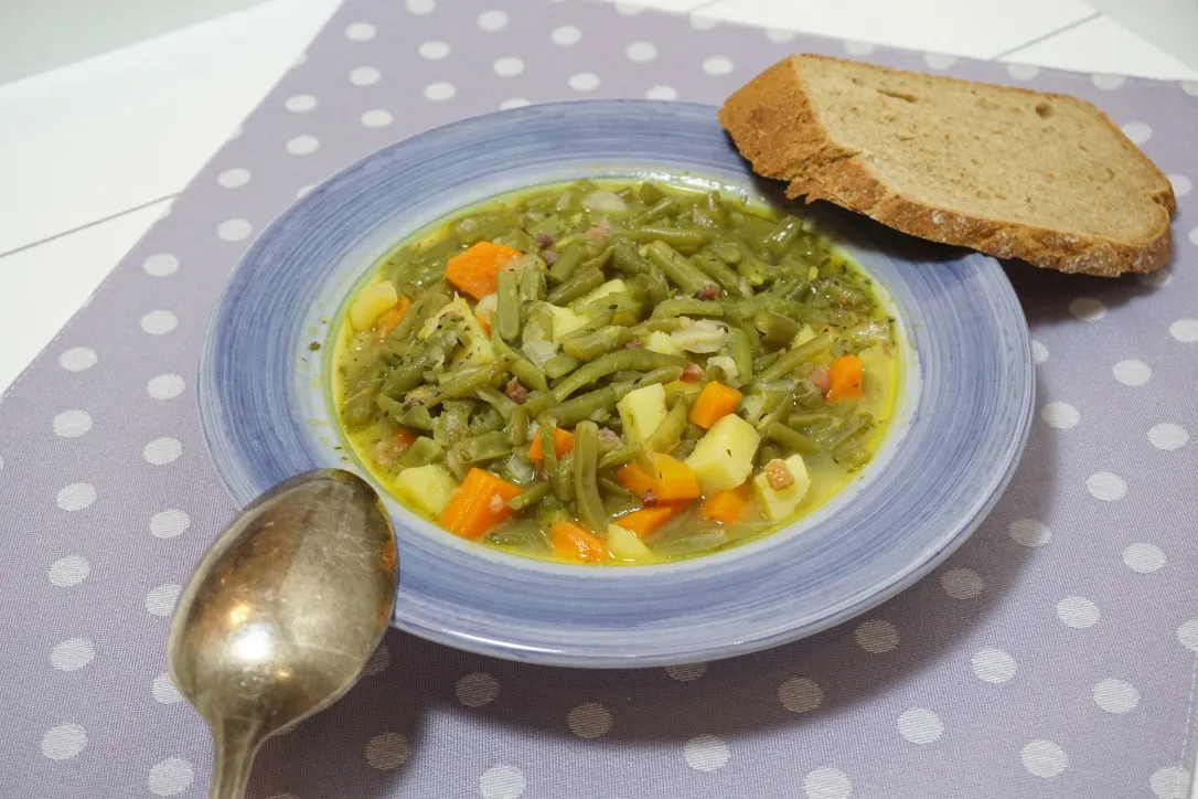 Ein Stück Joghurtbrot auf einem Teller, daneben eine Schale mit Bohneneintopf