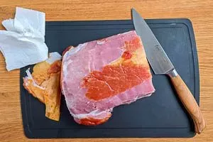 Ein Stück Kassler wird abgetupft und die Sehne entfernt, um es für die Zubereitung im Ofen vorzubereiten.