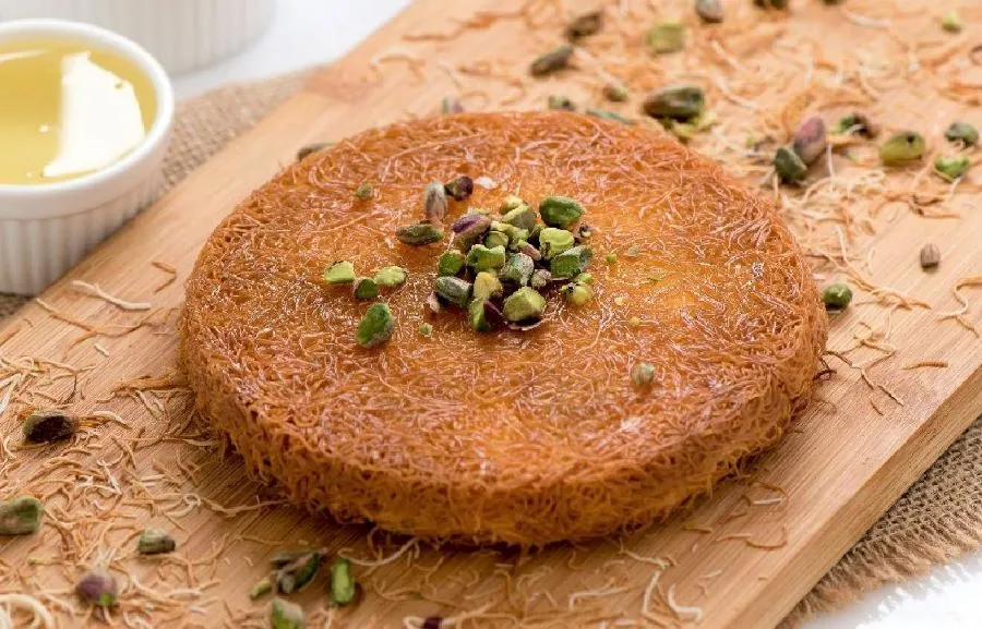 Ein Stück Kunafa mit feinen nudelartigen Fäden, gefüllt und mit süßem Sirup übergossen, auf einem Teller