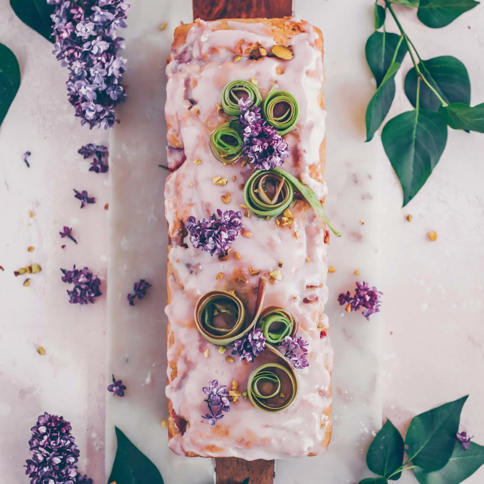 Ein Stück veganer Rhabarber-Joghurt-Kuchen auf einem Teller mit Fliederblüten