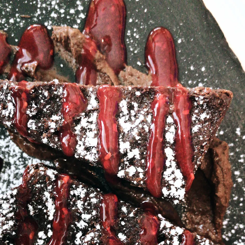 Ein Stück veganer Schokokuchen mit Beerensauce, appetitlich angerichtet auf einem Teller