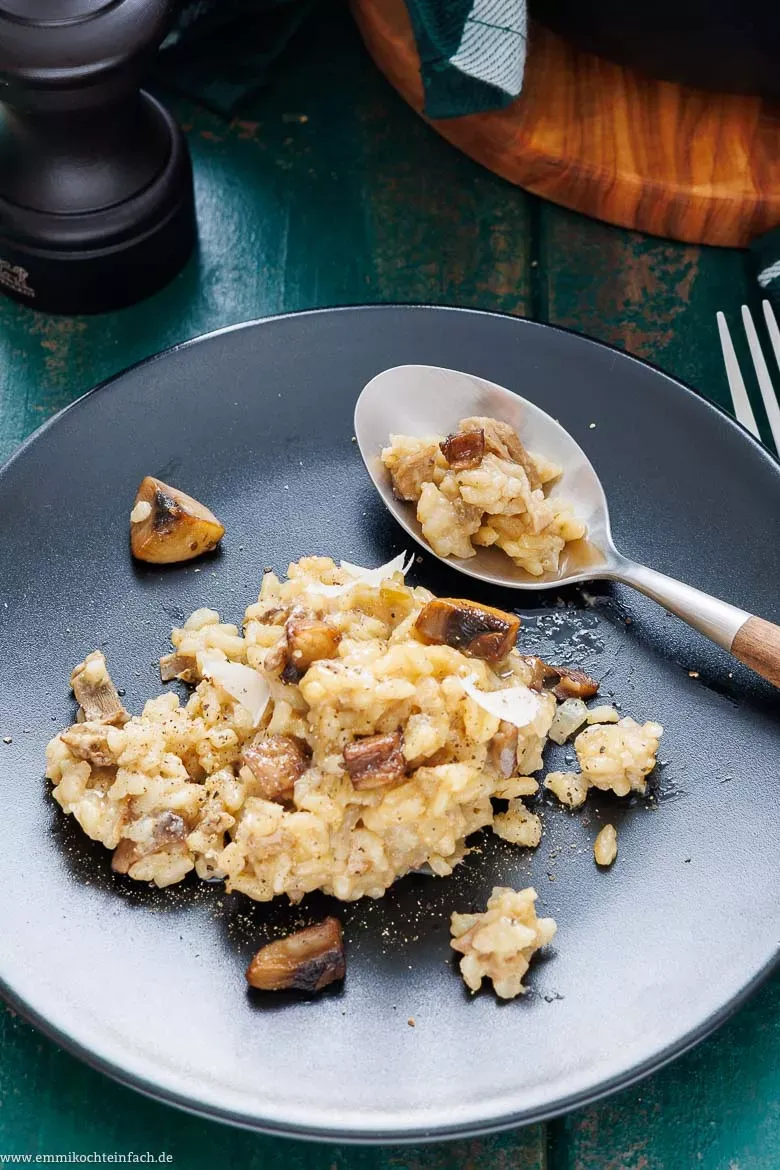 Ein Teller dampfendes Pilzrisotto wird mit frischen Kräutern garniert und serviert.