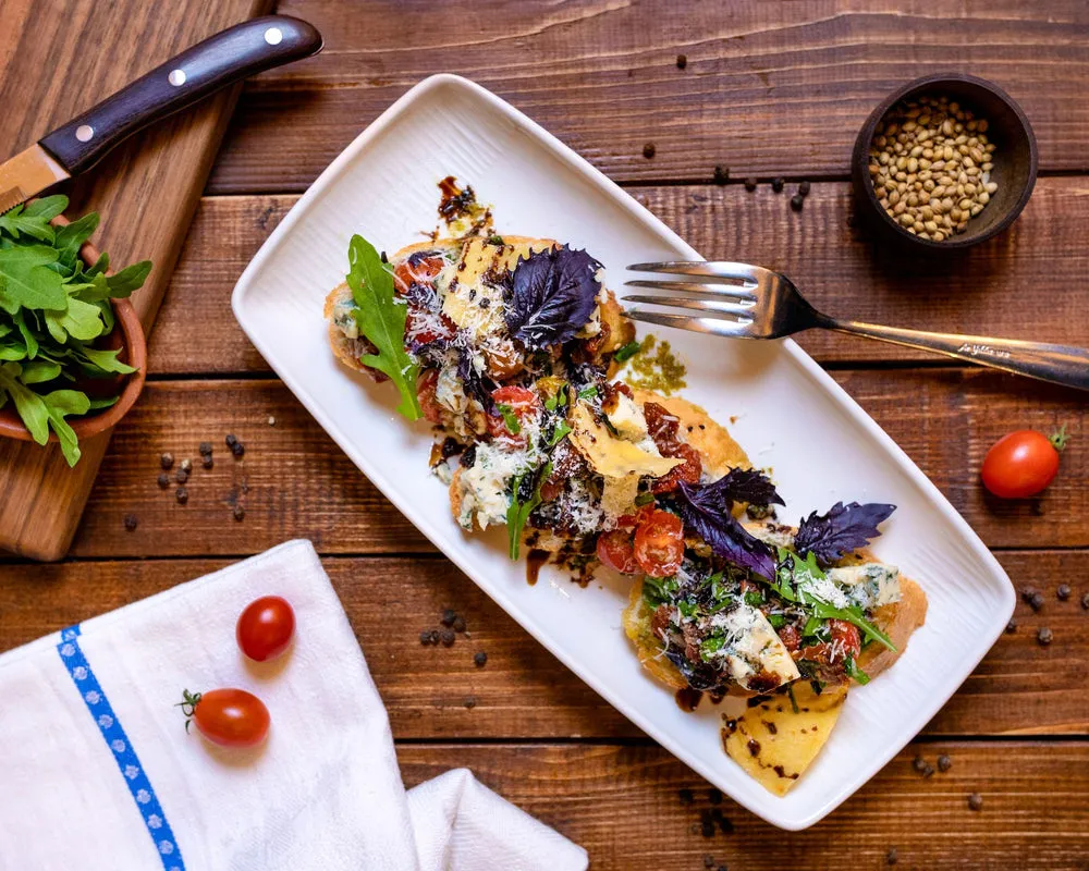 Ein Teller Haferbrei, garniert mit Beeren und Nüssen, steht auf einem Holztisch neben einer Tasse Tee.