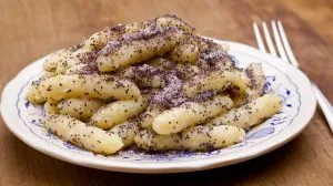 Ein Teller Hefenudeln mit Mohn und Puderzucker auf einem Holztisch.