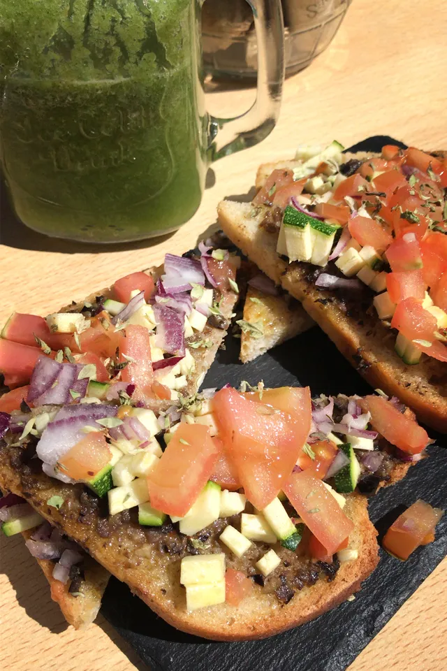 Ein Teller mit Bruschetta, belegt mit Zucchini, Oliven und Tomaten, als frischer, veganer Snack