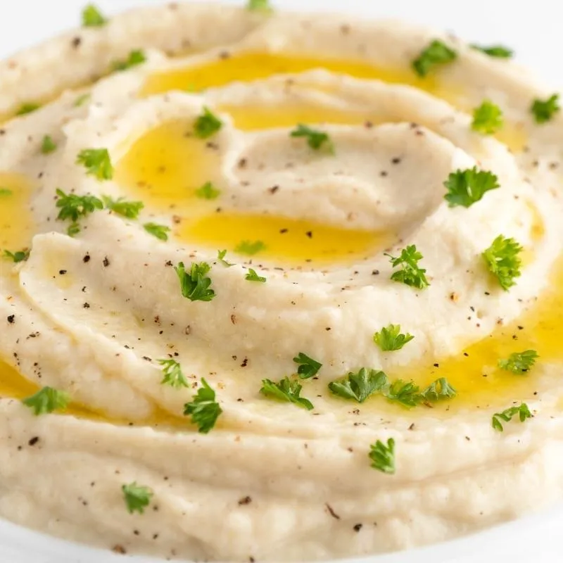 Ein Teller mit cremigem Keto Blumenkohl-Püree, garniert mit frischen Kräutern. Das Püree hat eine feine Konsistenz und eine appetitliche Farbe. Alt-Text: Keto Blumenkohl-Püree Rezept - Eine leckere und kohlenhydratarme Alternative zu Kartoffelpüree