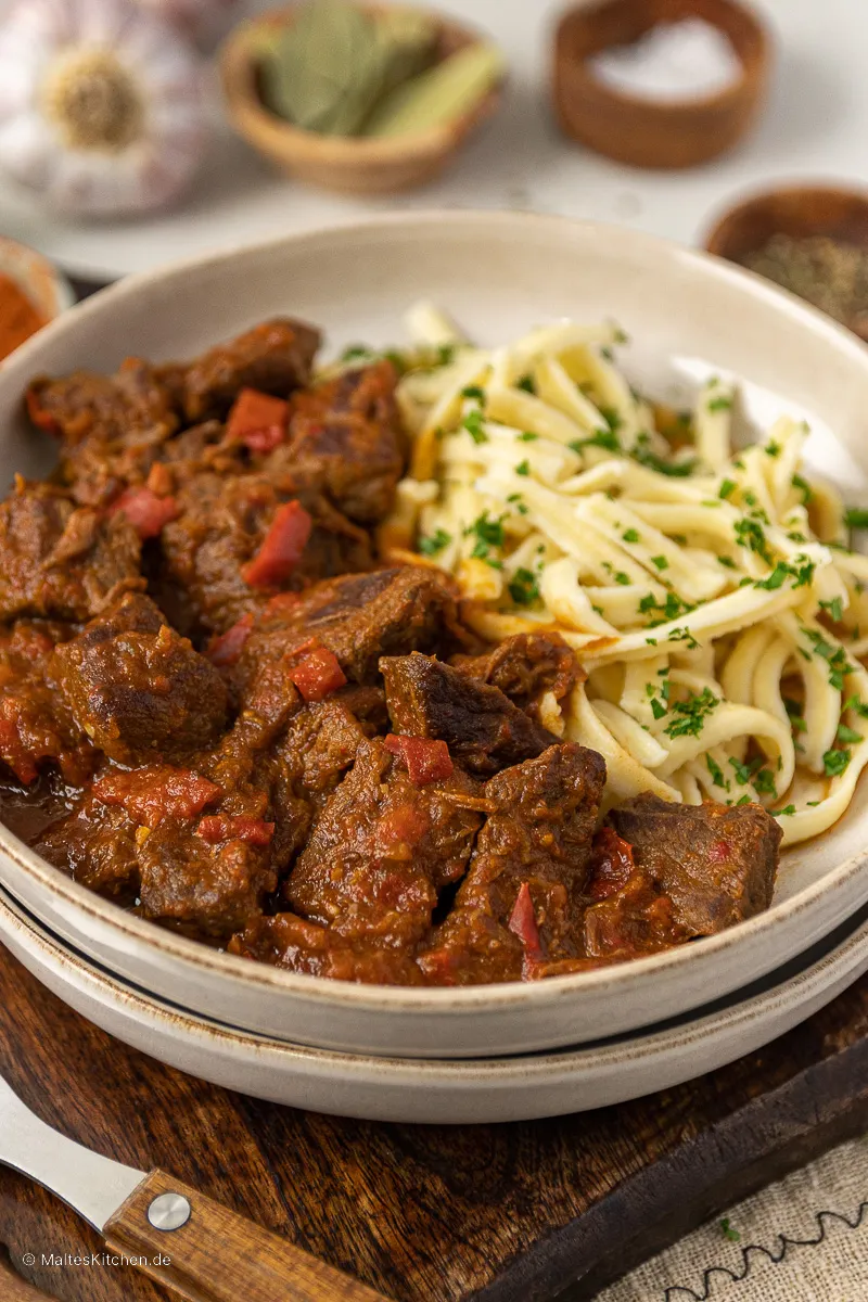 Ein Teller mit saftigem ungarischem Gulasch, serviert mit frischen Spätzle und Petersilie als klassische deutsche Beilage.