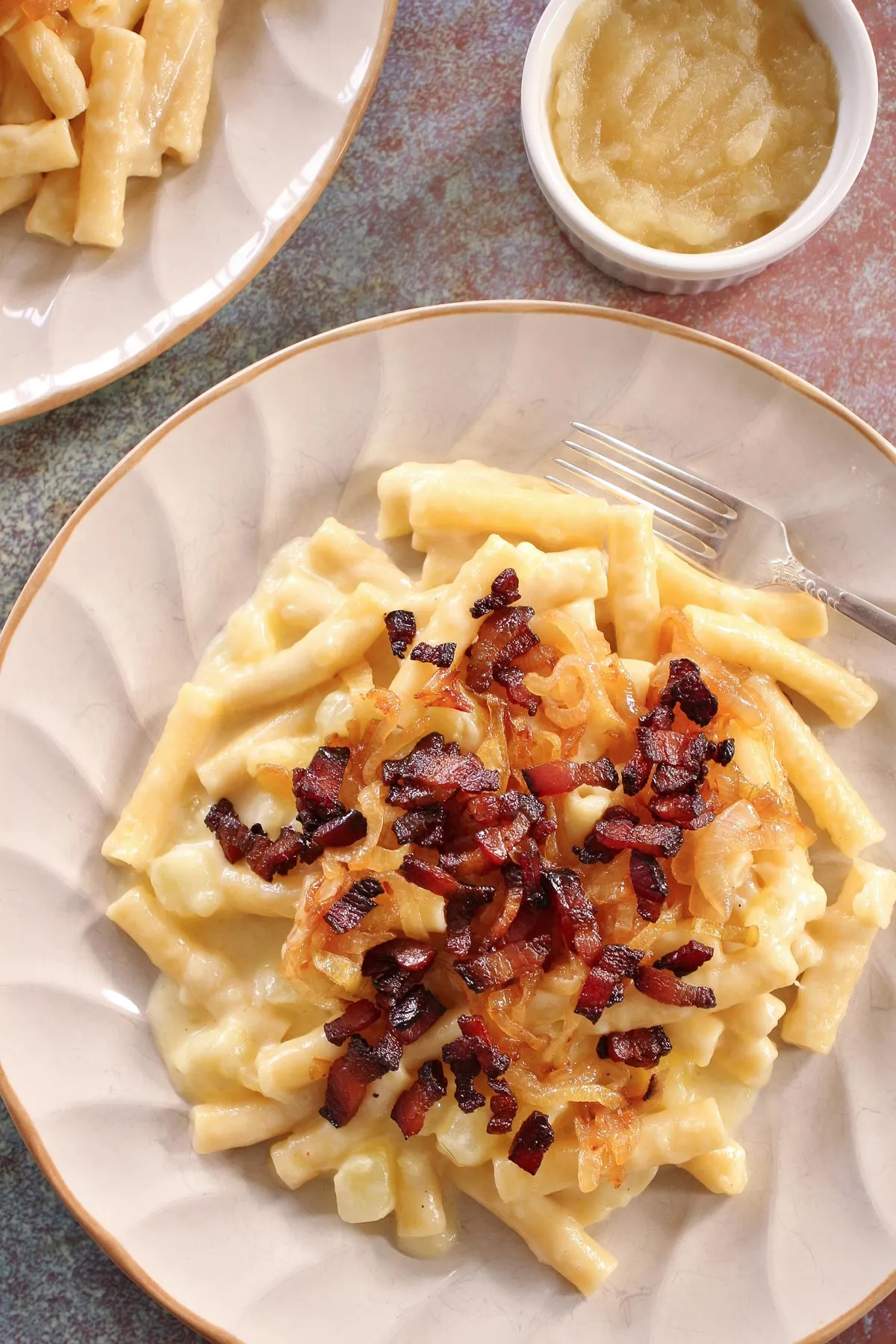 Ein Teller Schweizer Alpen-Makkaroni mit Speck und einer Beilage Apfelmus.
