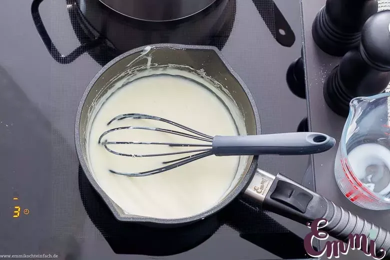 Ein Topf mit cremiger Béchamel, die dampfend auf dem Herd steht.