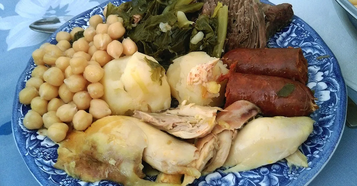 Ein traditioneller Cocido Madrileño, ein kräftiger Kichererbseneintopf mit verschiedenen Fleischsorten wie Chorizo, Blutwurst und Speck, serviert in einer rustikalen Tonschale