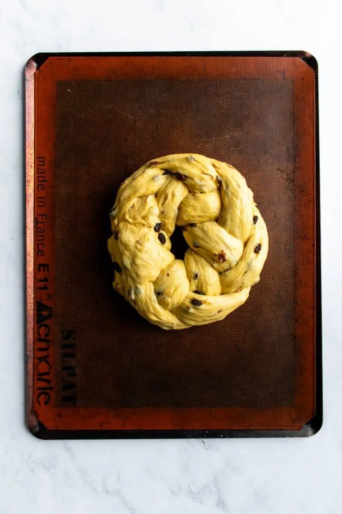 Ein ungebackener, geflochtener Osterkranz-Teigling auf einem Backblech, bereit zum zweiten Gehen und anschließendem Backen.