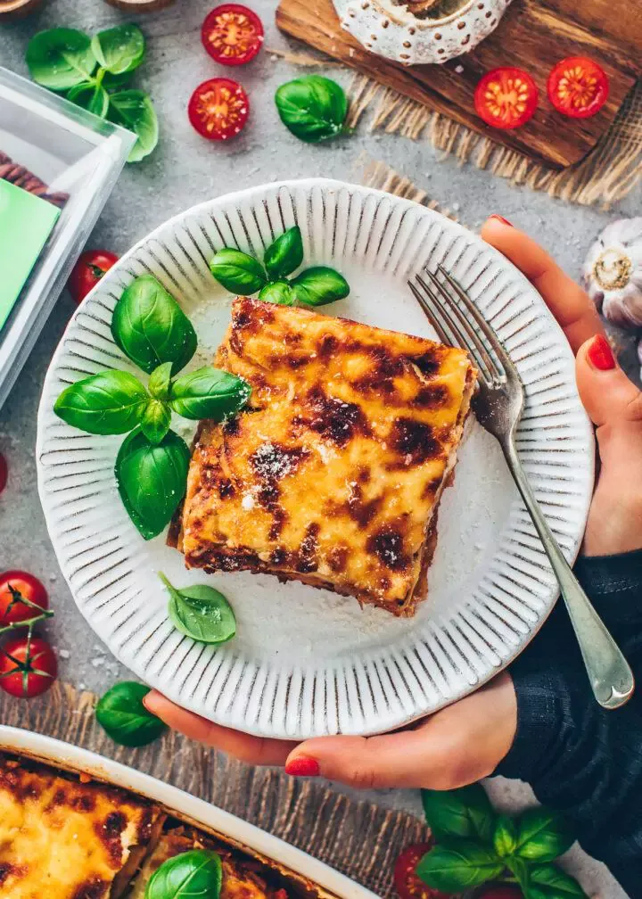 Ein weiteres Gericht veganer Lasagne mit einer dicken Schicht Béchamelsauce und goldbrauner Kruste, garniert mit frischem Basilikum.