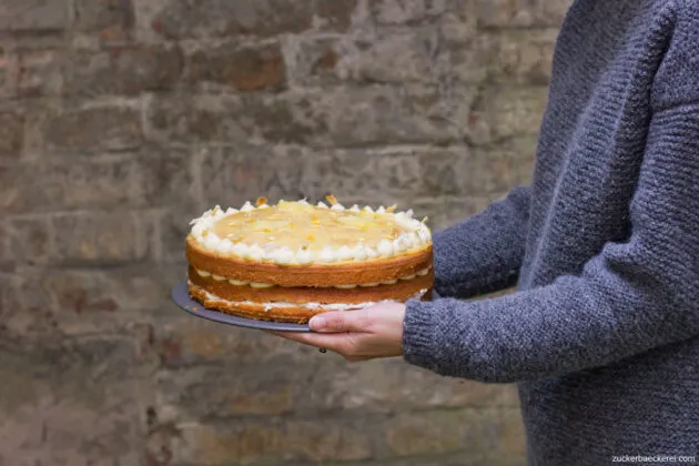 Eine Ananastorte in den Händen der Bäckerin, umrahmt von einer grauen Ziegelwand