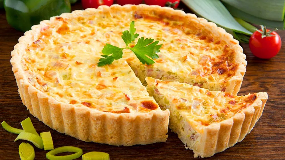 Eine angeschnittene Quiche Lorraine mit cremiger Füllung und knusprigem Rand.