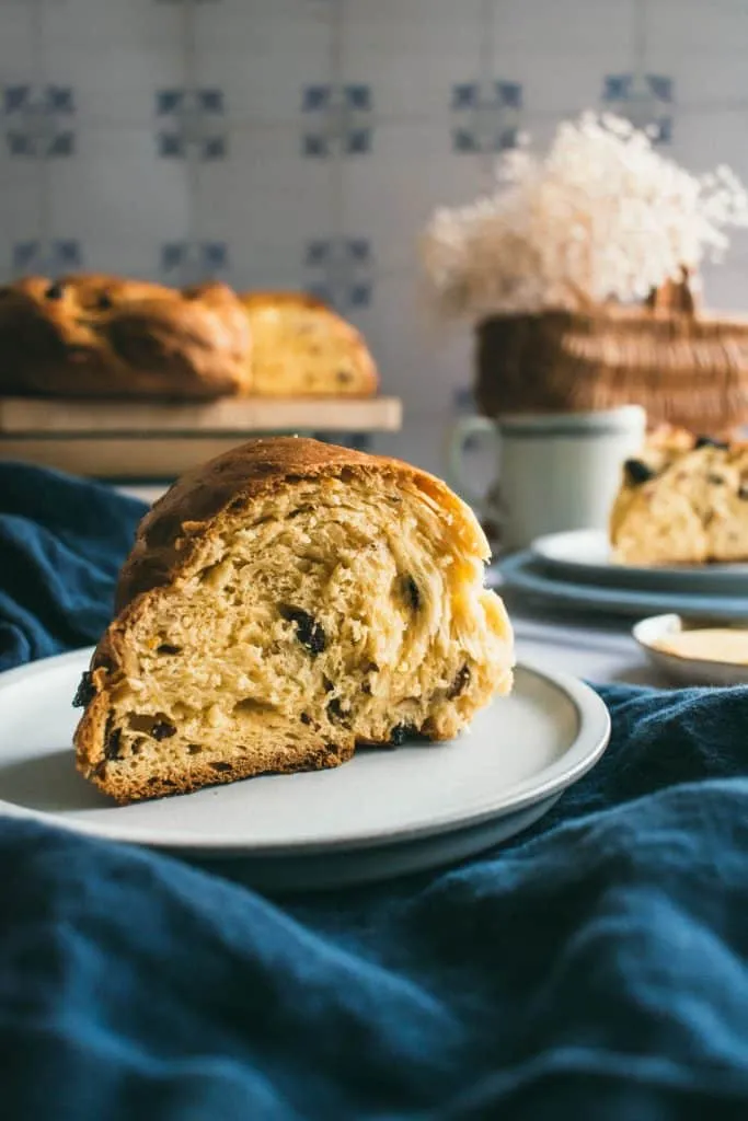 Eine angeschnittene Scheibe des süßen Osterkranzes, die die saftigen Rosinen und Mandeln im Inneren des Gebäcks zeigt, auf einem kleinen grauen Teller.