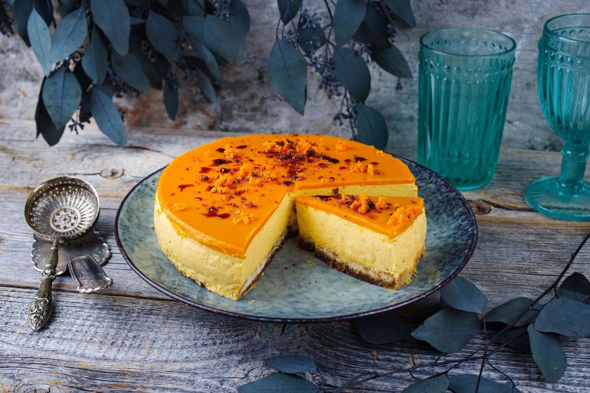 Eine appetitliche Sanddorn Sahne Torte auf einem blauen Teller im nordischen Design, mit bereits entnommenen Stücken, die die cremige Textur und die leuchtende Farbe hervorheben.