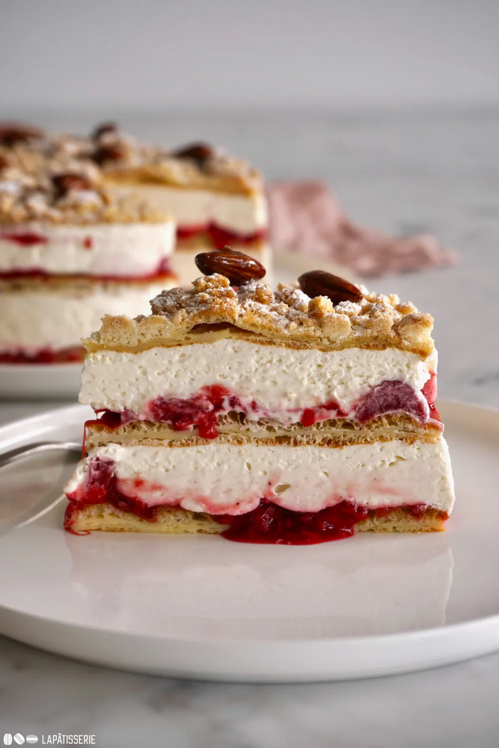 Eine aufgeschnittene Flockensahnetorte mit Vanillecreme, Rhabarber-Himbeer-Kompott und knusprigen Streuseln