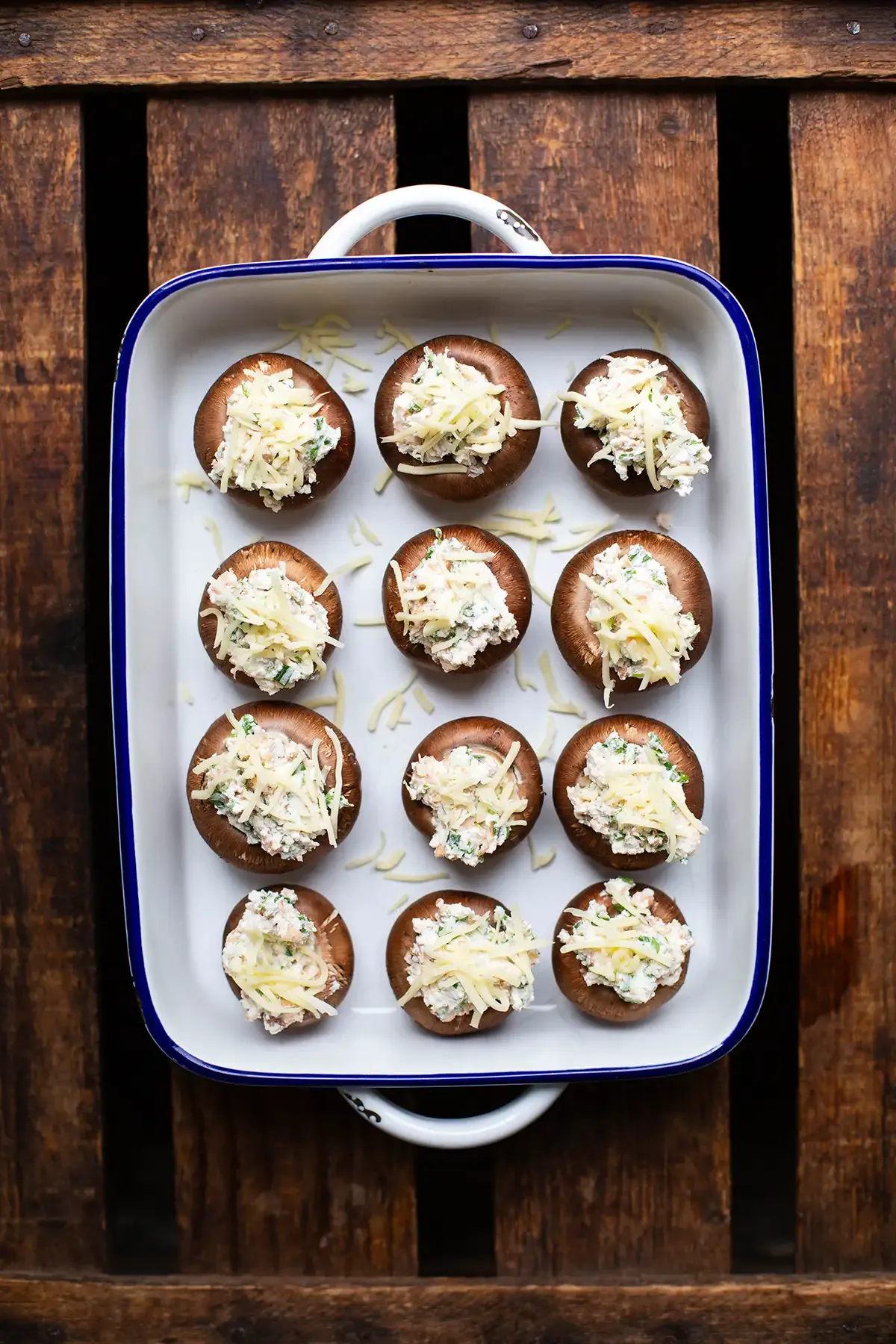 Eine Auflaufform mit zwölf vorbereiteten, vegetarisch gefüllten Champignons, bereit für den Backofen oder Grill.