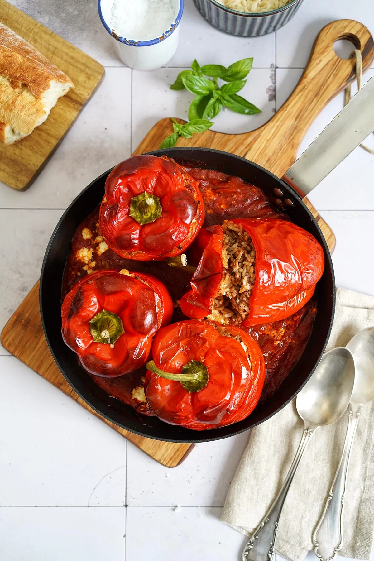 Eine Auflaufform voller gefüllter Paprika, die mit Tomatensoße übergossen und mit Feta bedeckt sind