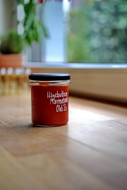 Eine Auswahl an frischen Hagebutten neben einem Glas Hagebuttenmarmelade