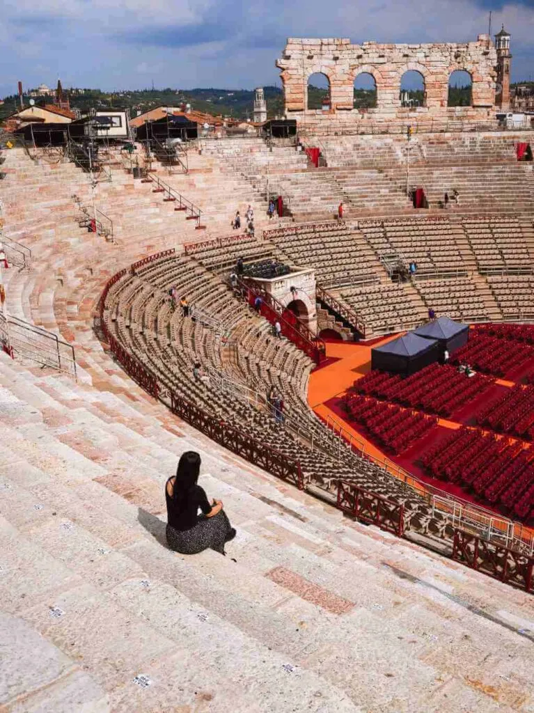 Eine Besucherin sitzt auf den Steinstufen in der römischen Arena von Verona. Das beeindruckende Amphitheater ist ein Zeugnis der römischen Geschichte und Kultur.
