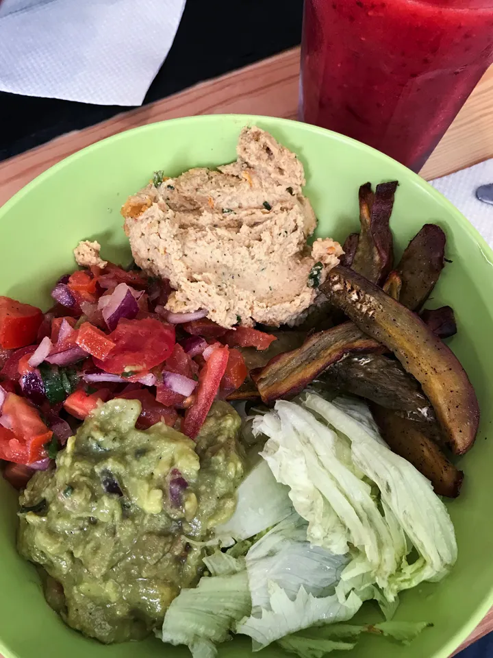 Eine Bowl mit Hummus, Süßkartoffeln, Guacamole, Salat, Quinoa und Pico de Gallo auf einem Holztisch