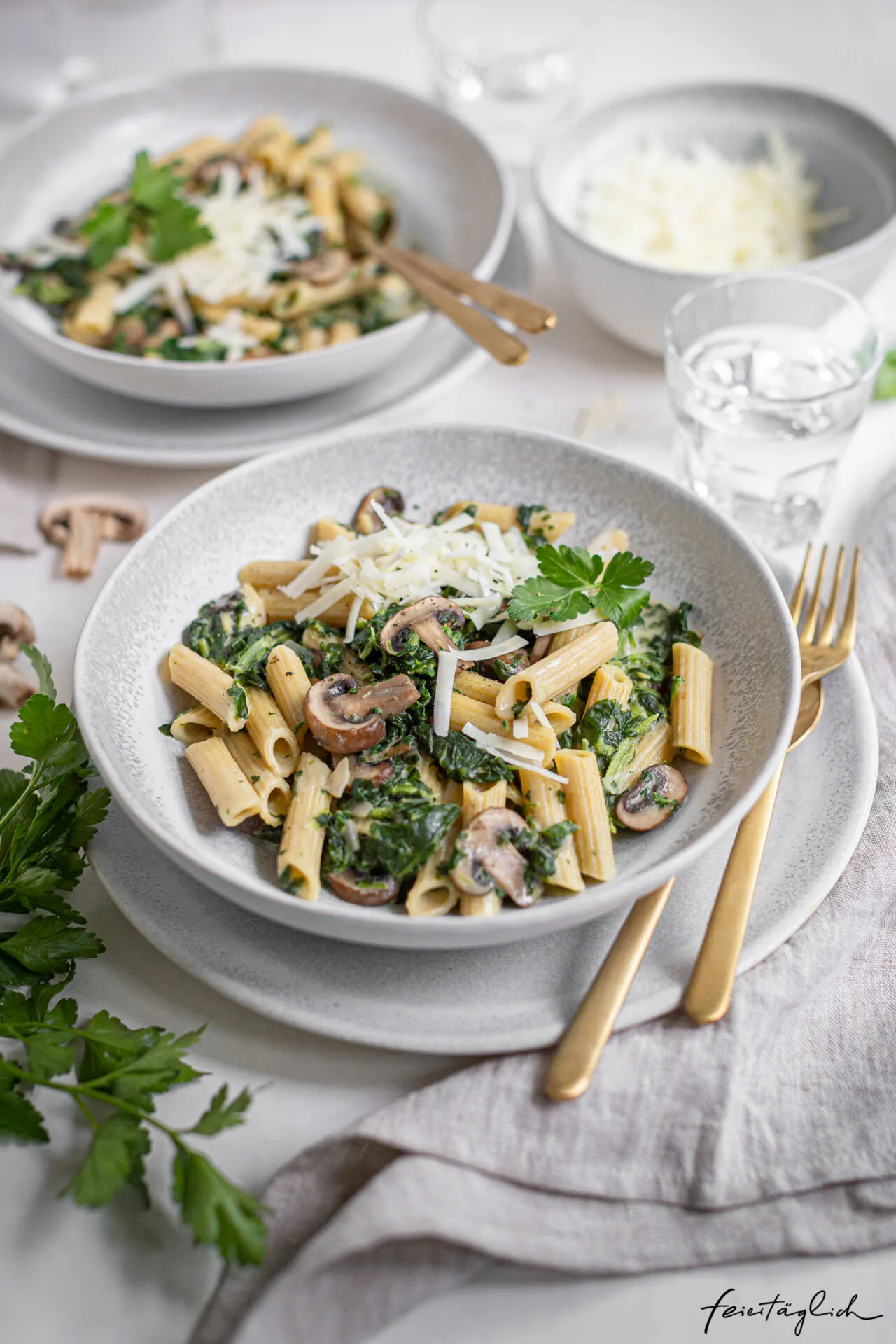 Eine dampfende Portion Pasta mit Spinat und Pilzen, garniert mit frisch geriebenem Pecorino.