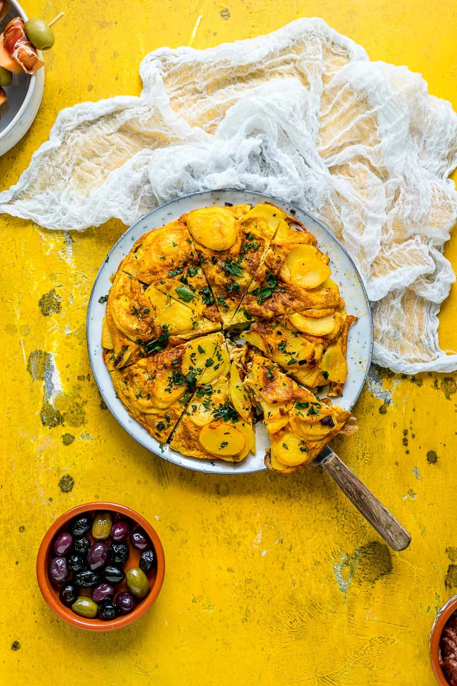 Eine detaillierte Aufnahme einer köstlichen spanischen Tortilla mit Kräutern als perfekte Beilage auf einer Tapas-Platte.