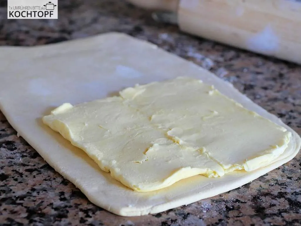 Eine dünn ausgerollte Butterplatte sorgfältig auf dem vorbereiteten Grundteig platziert, bereit zum Einschlagen für deutschen Blätterteig.