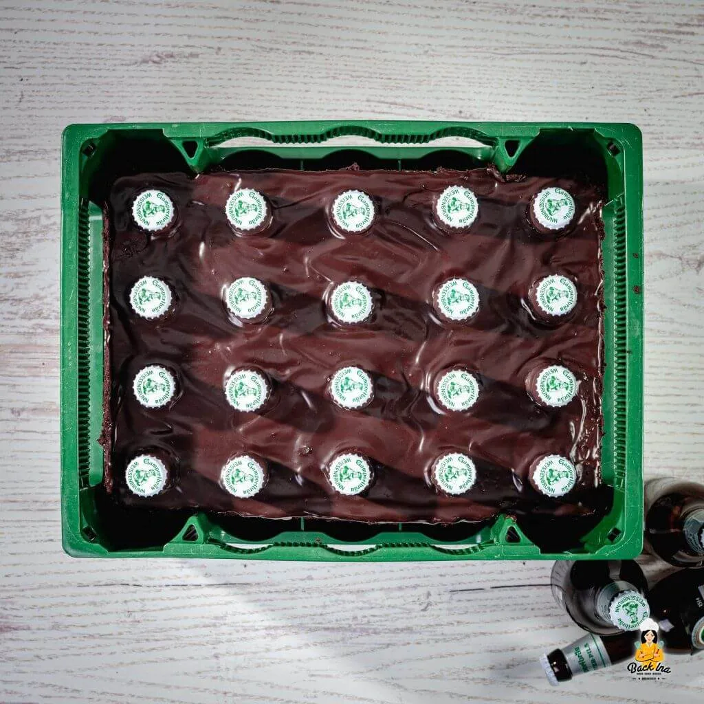 Eine fertige Bierkasten-Torte steht auf einem Tisch, dekoriert mit Kronkorken und Schokoladenflaschen, bereit zum Servieren.