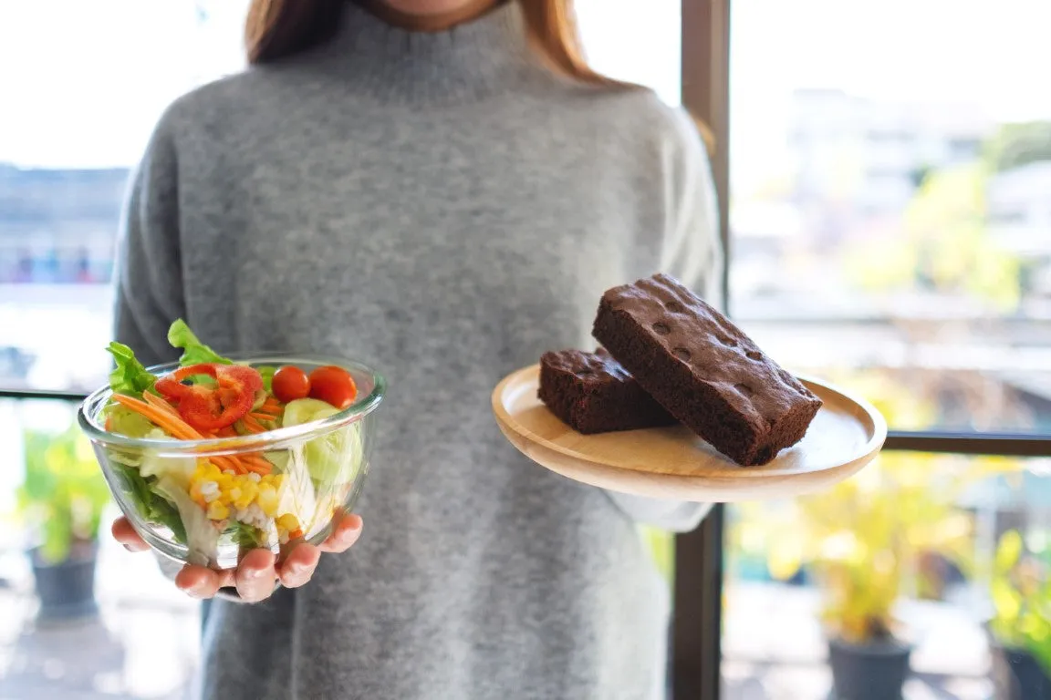 Eine Frau hält in einer Hand eine Schüssel mit Salat und in der anderen Hand ein Zeller mit zwei großen Brownie Stücken