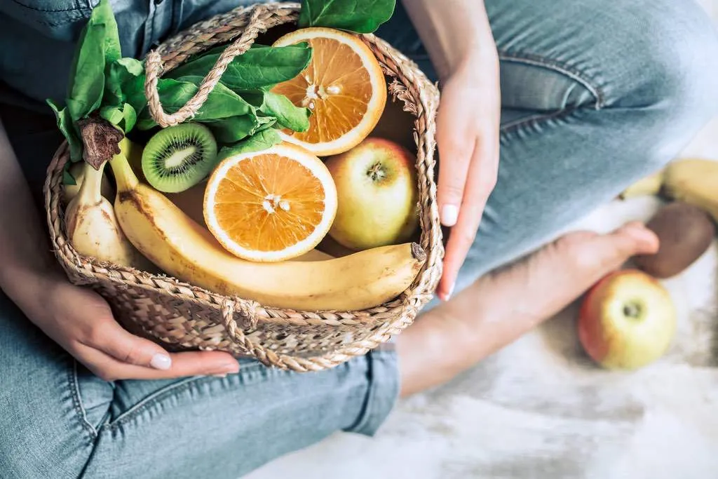 Eine Frau lächelt und hält einen Korb voller frischem Obst und Gemüse