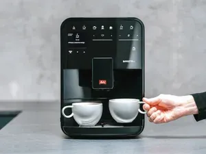 Eine Frau nimmt eine Tasse Kaffee aus der Melitta Barista SE, die auf einer Küchenarbeitsplatte steht.