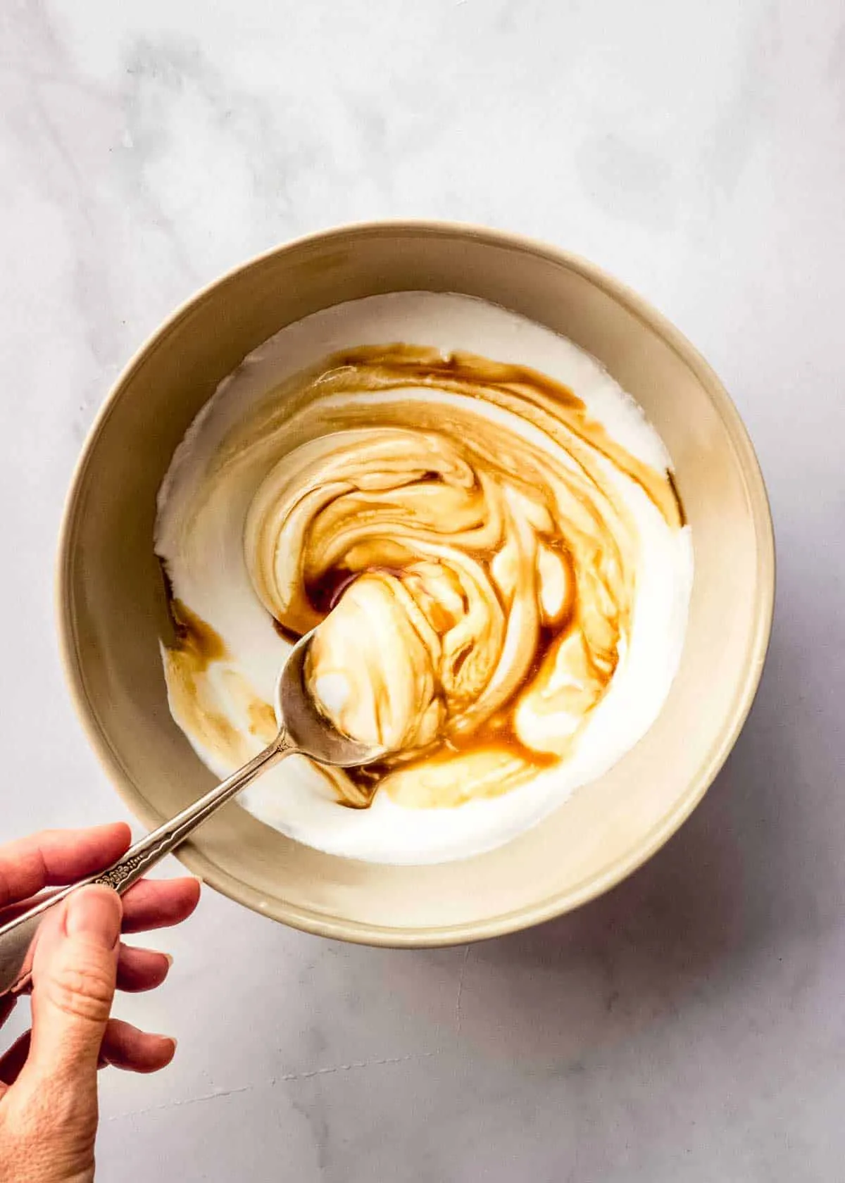 Eine Frau rührt in einer braunen Schüssel Kokosjoghurt, Ahornsirup und Vanilleextrakt um.