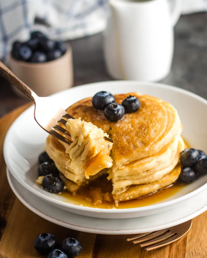 Eine Gabel nimmt einen Bissen von einem Pancake, getoppt mit Sirup und Blaubeeren.