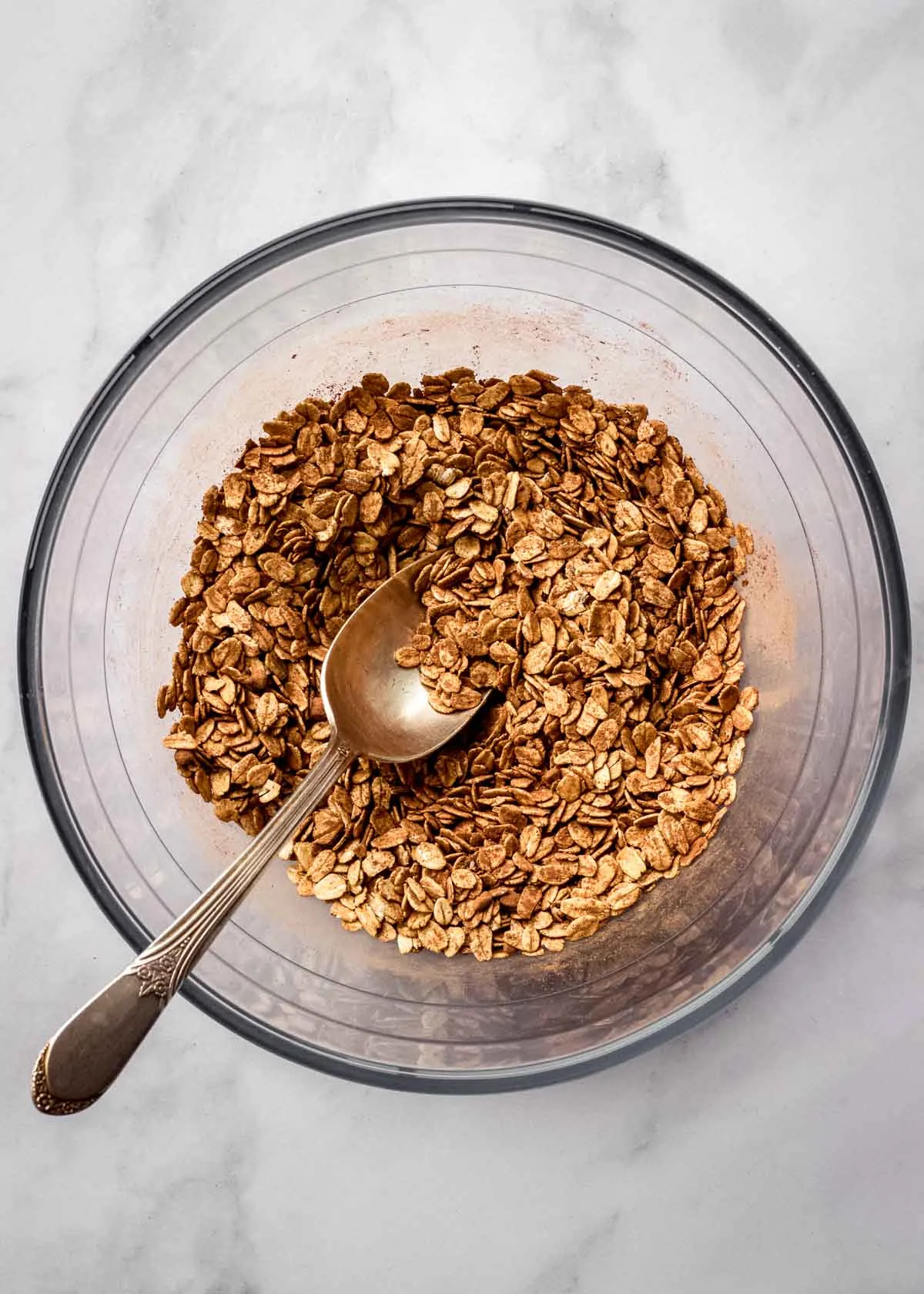 Eine große Glasschüssel mit Haferflocken, Kakaopulver und Chiasamen, daneben ein Metalllöffel.