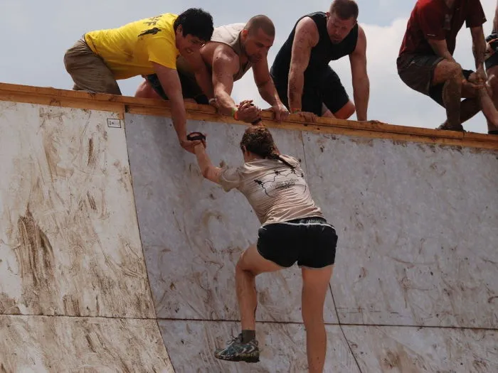 Eine Gruppe von Teilnehmern überwindet gemeinsam ein schlammiges Hindernis mit Seilen bei einem Tough Mudder Event