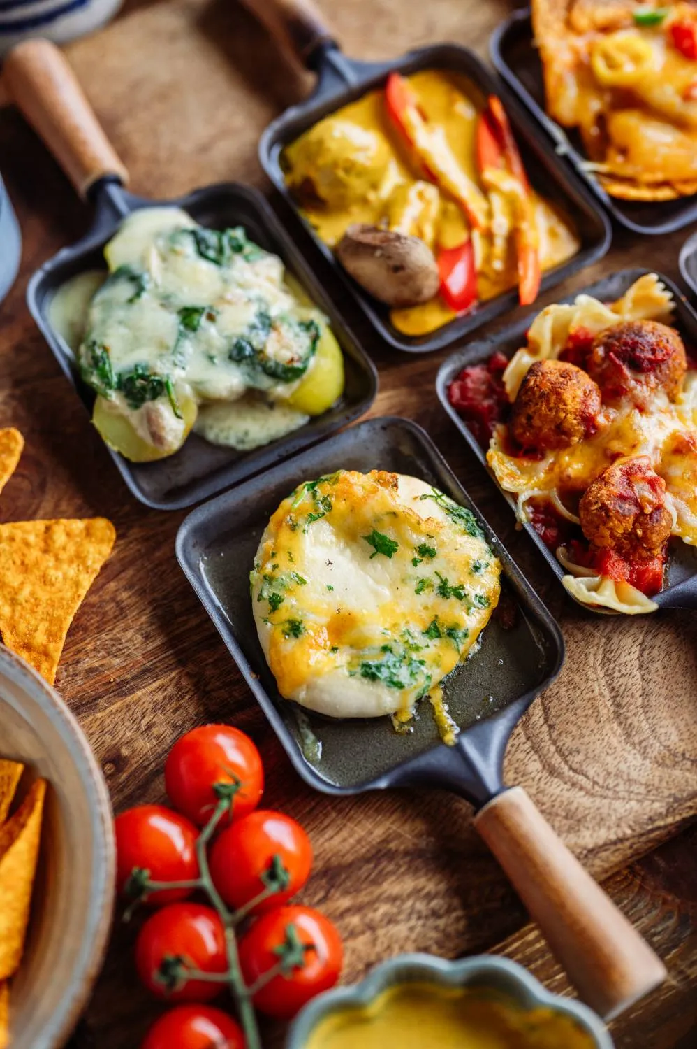 Eine Hand belegt eine kleine Pizza in einem Raclette-Pfännchen mit frischen Zutaten